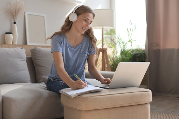 Smiling girl sit near couch watching webinar on laptop. Happy young woman study on online distant course.