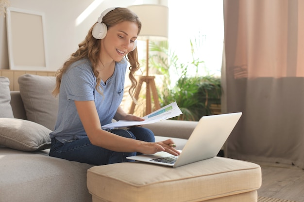 Smiling girl sit near couch watching webinar on laptop. Happy young woman study on online distant course.