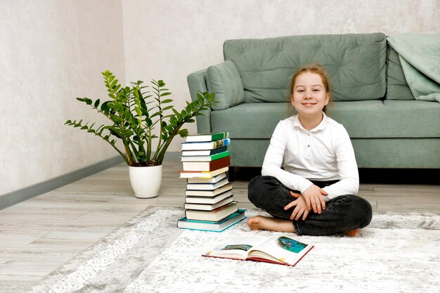 smiling girl sitting on the floor next to a stack of books at home