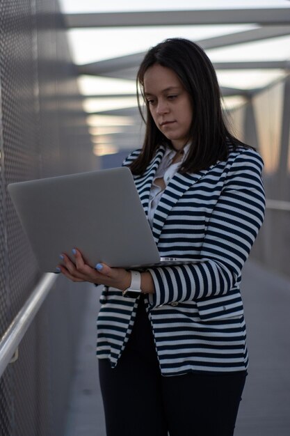 Smiling girl standing using laptop on a bridge Smiling woman standing using laptop on the corridor of a bridge Concept of female entrepreneur using laptop on a bridge