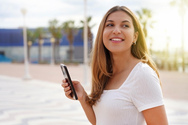 Smiling girl strolling alone holding phone at sunset on summer