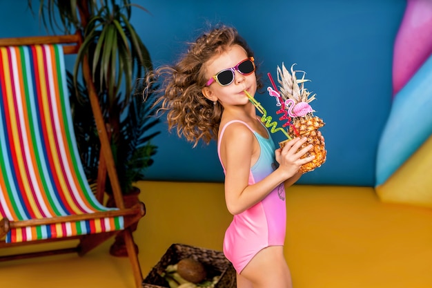 Smiling girl in swimsuit and sunglasses stay near rainbow deck c