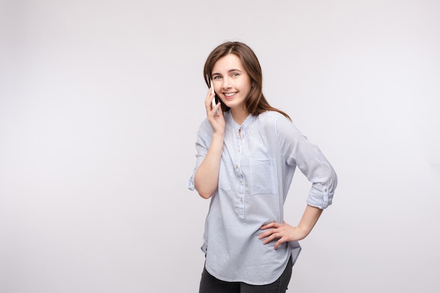 Smiling girl talking on the phone.Pretty young brunette woman in casual shirt and jeans talking on the mobile phone and smiling at camera. Isolate on white.