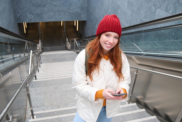 Smiling girl walking on stairs using mobile phone texting message on her way using smartphone app ma