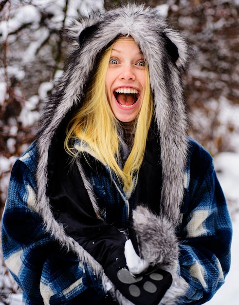 Smiling girl in warm clothing with snowball beautiful young woman playing with snow in winter park