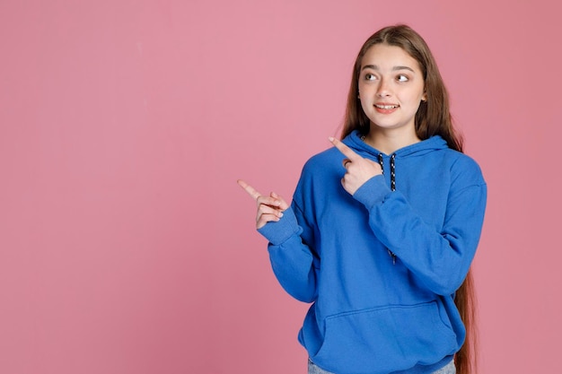 Smiling girl with long fair hair pointing away with fingers showing direction while looking up