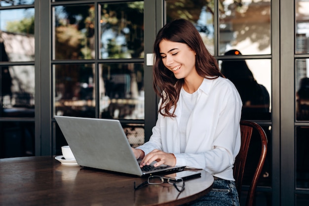 Smiling girl working at laptop in cafe