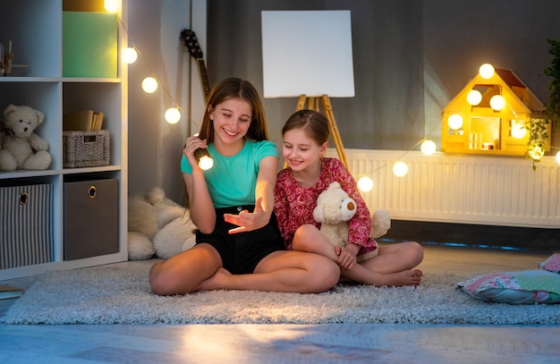 Smiling girls making hand shadow theatre using flashlight in kids room