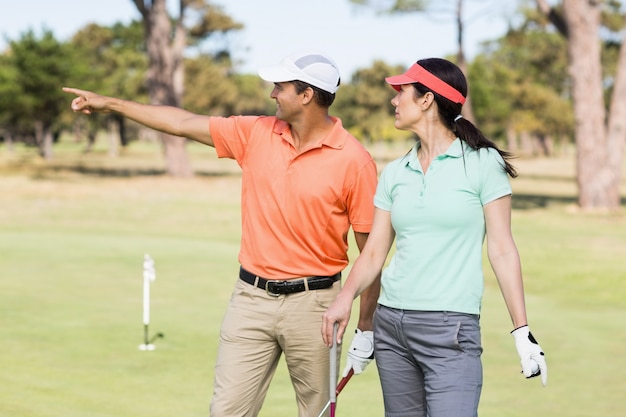 Smiling golfer man pointing while standing by woman