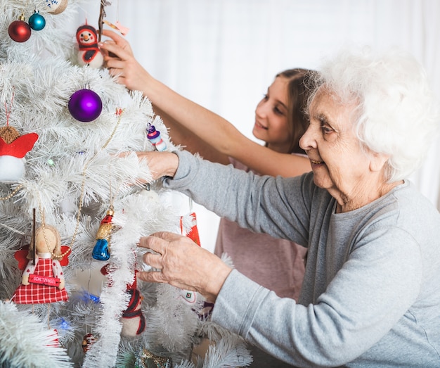 Smiling granddaughter with grandma decorating fancy Christmas tree