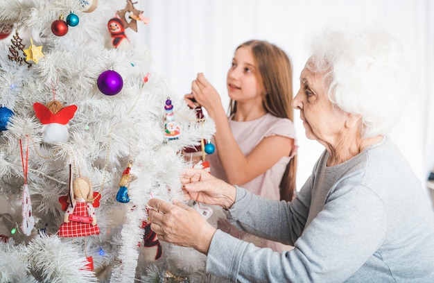 Smiling granddaughter with grandma decorating fancy Christmas tree