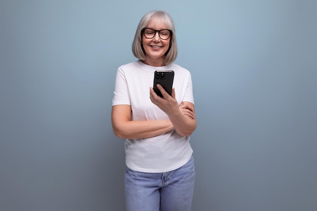 Smiling grayhaired mature woman communicates on the internet in a smartphone on a bright studio