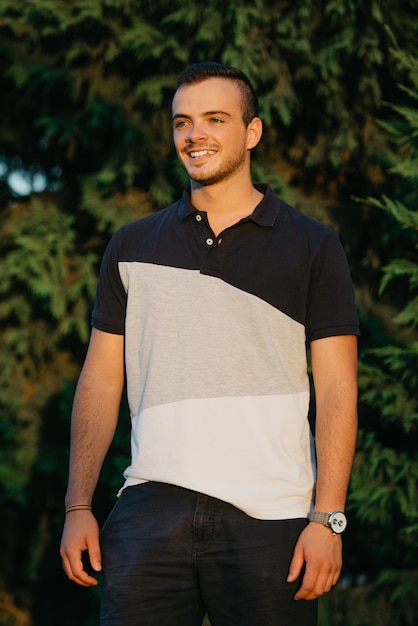 A smiling guy is posing with green bushes in the background