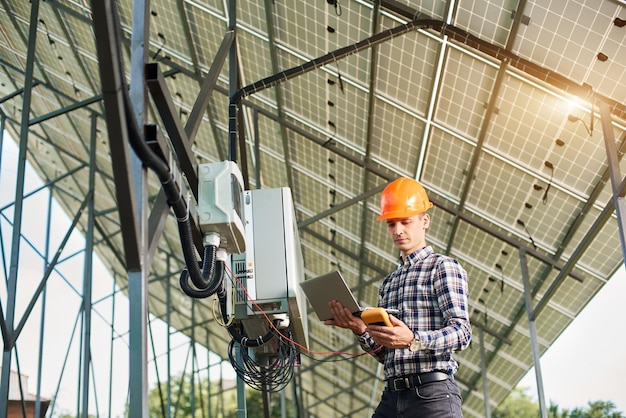 Smiling guy with laptop and sensor in the background of the solar power station