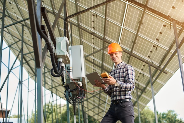 Smiling guy with laptop and sensor in the background of the solar power station