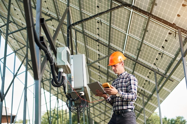 Smiling guy with laptop and sensor in the background of the solar power station