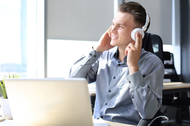 Smiling handsome businessman relaxing and listening music in earphones in a modern office.