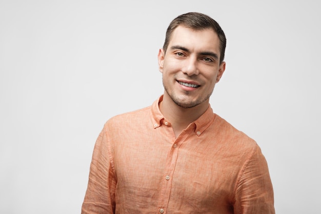 Smiling handsome caucasian man about 30 years old in orange shirt on grey background male portrait