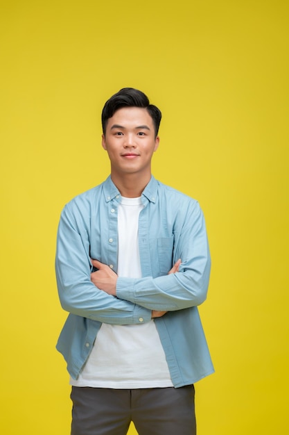 Smiling handsome man in blue polo shirt standing with crossed arms isolated on yellow background