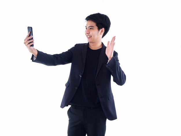 Smiling handsome man with smartphone having video call and waving hand while standing on white