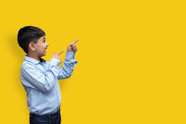 Smiling happy boy pointing finger away at copy space isolated over plain background