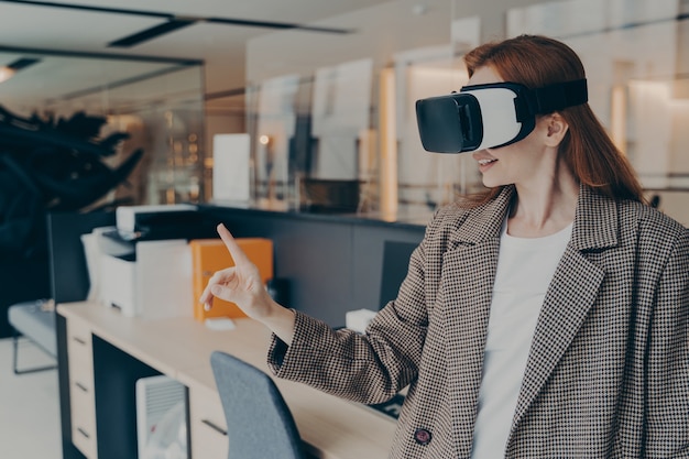 Smiling happy businesswoman wearing vr headset trying out virtual reality for first time at work