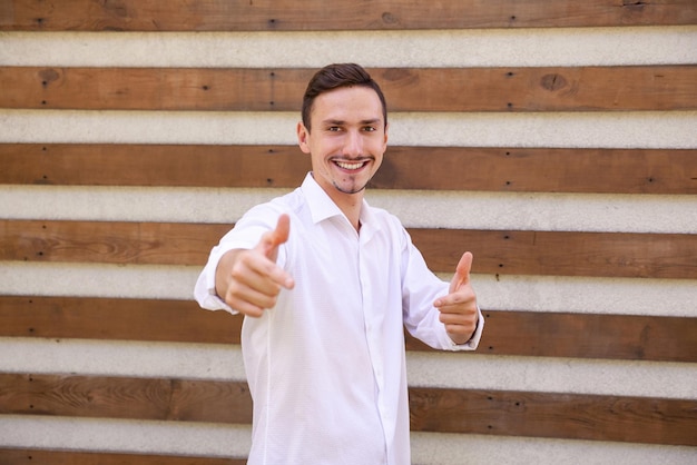 Smiling happy Caucasian guy pointing fingers and looking at the camera on a brown ribbed