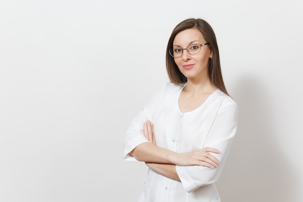 Smiling happy confident attractive young doctor woman with glasses isolated on white background. Female doctor in medical gown holding hands crossed. Healthcare personnel, health, medicine concept.