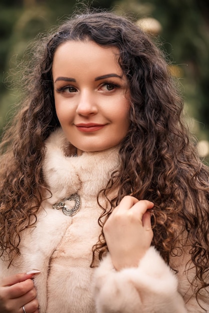 Smiling happy curlyhaired woman in a fur coat strolls through the Christmas tree fair Waiting for Christmas and New Year