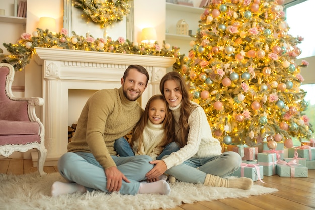 Smiling happy family sitting on the floor near Christmas tree