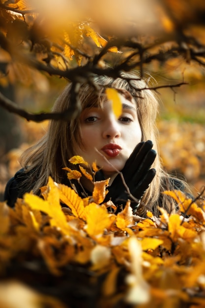 Smiling happy girl portrait with autumn leaves. Young woman among golden autumn leaves. Romantic moment in warm light. Park with yellow leaves and autumn atmosphere.