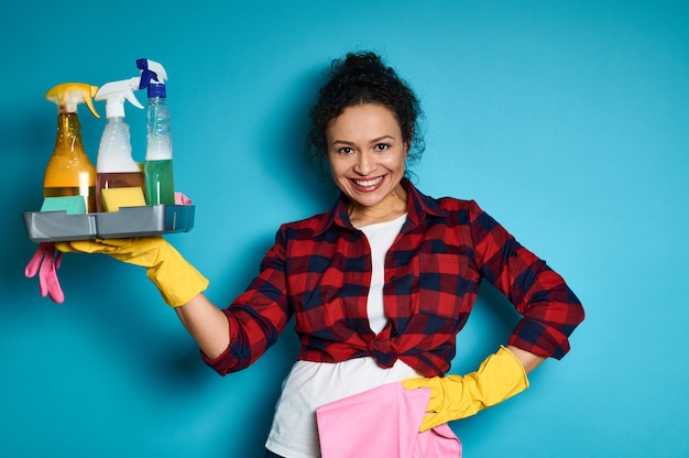 Smiling and happy Latin American woman raising her arm up with tray full of chemical cleaning products in the hand