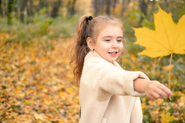 smiling happy little child girl in coat and dress holding autumn leaves, having fun in fall forest