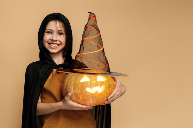 Smiling happy little girl wearing witch costume holding jackolantern for halloween