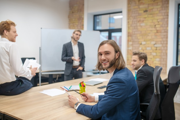 Smiling happy man in blue jacket turning to camera and colleagues communicating after presentation