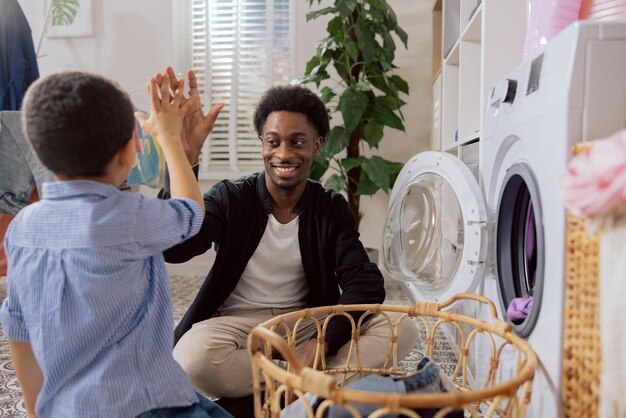 Smiling happy men sitting on the laundry room floor next to the washing machine throwing clothes