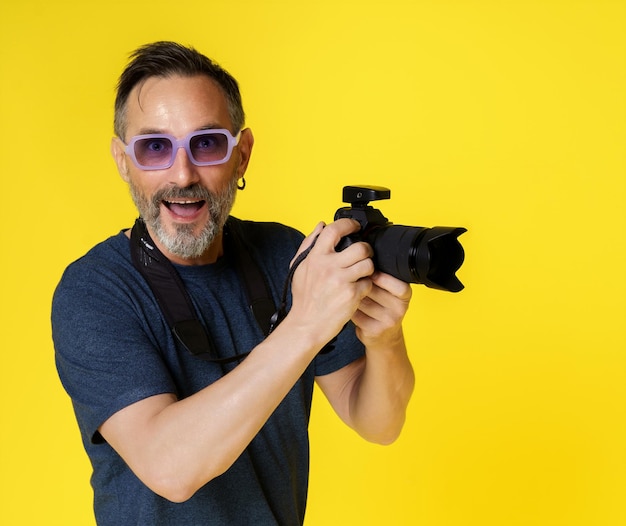 Smiling and happy midaged man passionate about photography isolated on yellow background holding