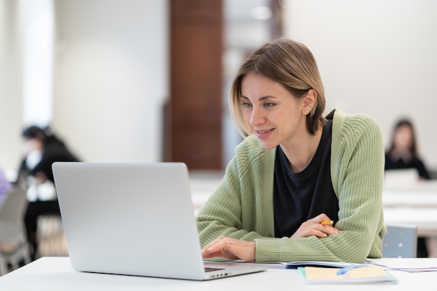 Smiling happy middleaged woman enjoying online study watching webinar via laptop in library