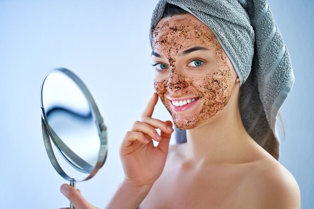 Smiling happy woman in bath towel with natural face coffee scrub mask after shower