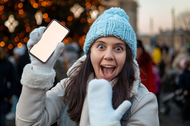 Smiling happy woman at christmas city fair holding phone with white screen