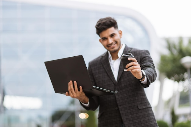 Smiling hindu man posing on camera while working on laptop outdoors office