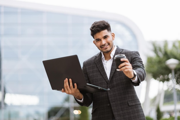 Smiling hindu man posing on camera while working on laptop outdoors office