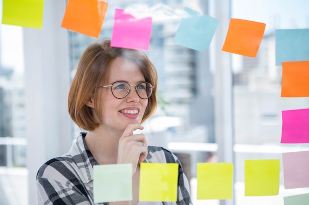 smiling hipster woman in her office, sticking notes to a wall