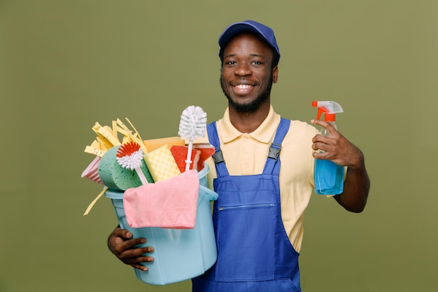 smiling holding bucket of cleaning tools young africanamerican cleaner male in uniform with gloves isolated on green background