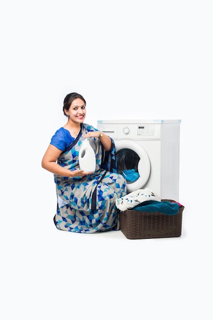 Smiling Indian Asian housewife in Saree Standing Near Washing Machine With Basket Of Clothes