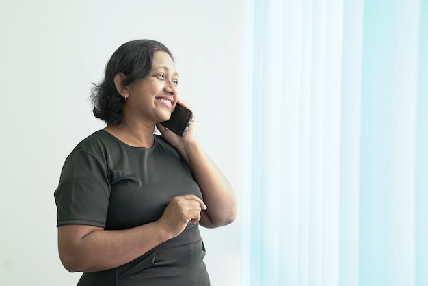 Smiling Indian corporate woman talking on her phone next to the office windows