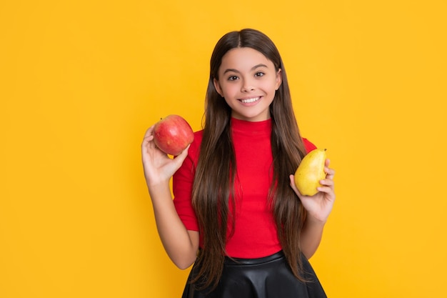 Smiling kid hold fresh apple and pear on yellow background