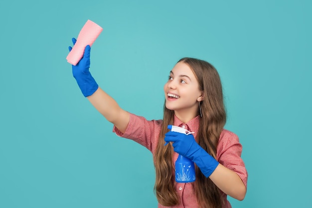 Smiling kid in rubber gloves with spray bottle and microfiber rag on blue background