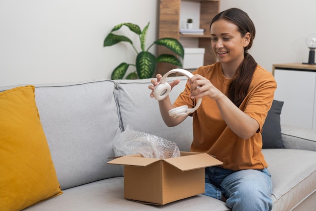 Photo smiling lady celebrates unwraps parcel containing modern headphones delivered from online store