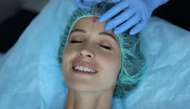 Smiling lady gets injection of botox in her forehead cosmetologist using syringe with liquid